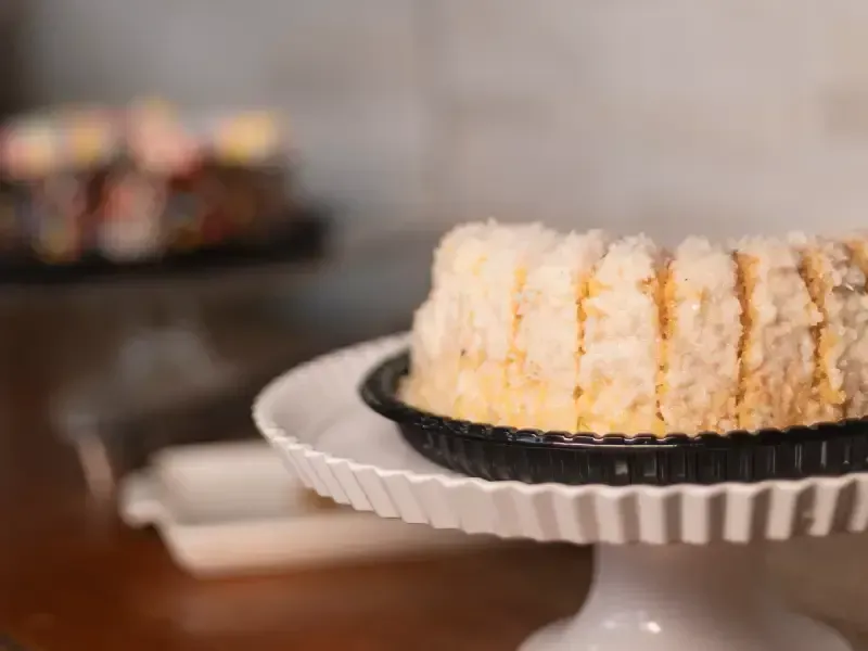 Bolo em um suporte branco, com outro bolo desfocado ao fundo.