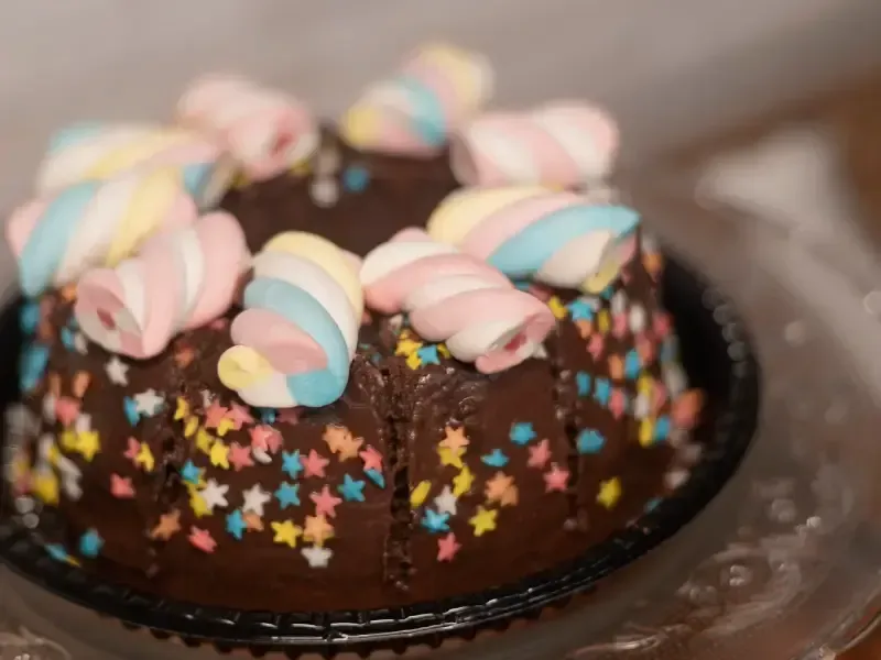 Bolo de chocolate com granulado colorido e marshmallows em espiral servido em um prato preto.