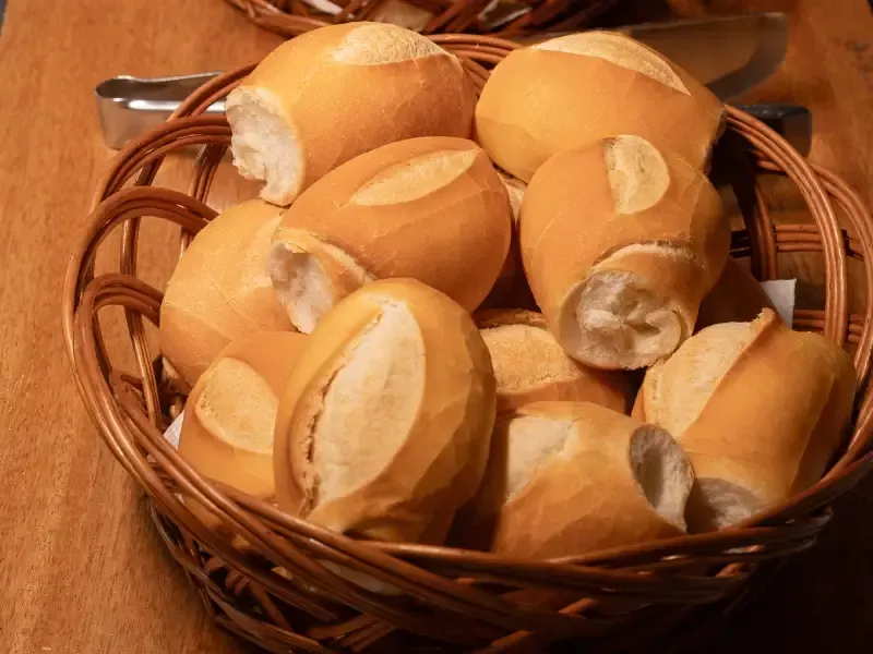 Cesta de pãezinhos dourados e crocantes sobre uma mesa de madeira.