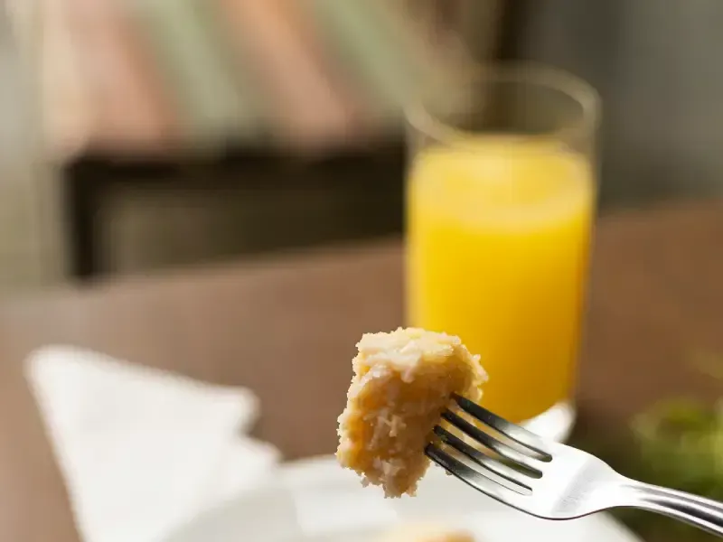 Garfo segurando um pedaço de comida dourada com um copo de suco de laranja.