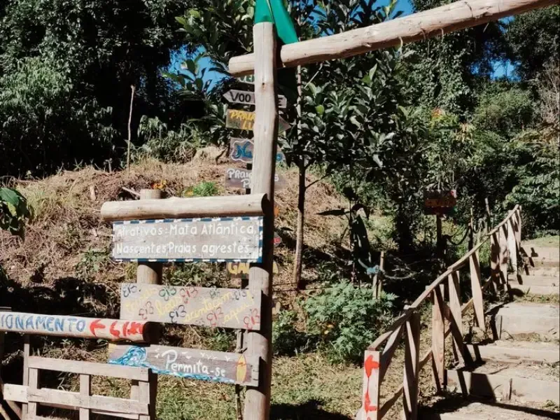 Placa de madeira com indicações na entrada de uma trilha que leva a um monumento e mirante, com degraus e corrimão de madeira.
