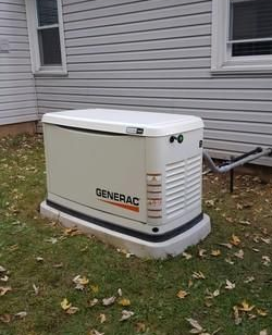 Generac generator next to a house with white siding and windows, on a patch of grass.
