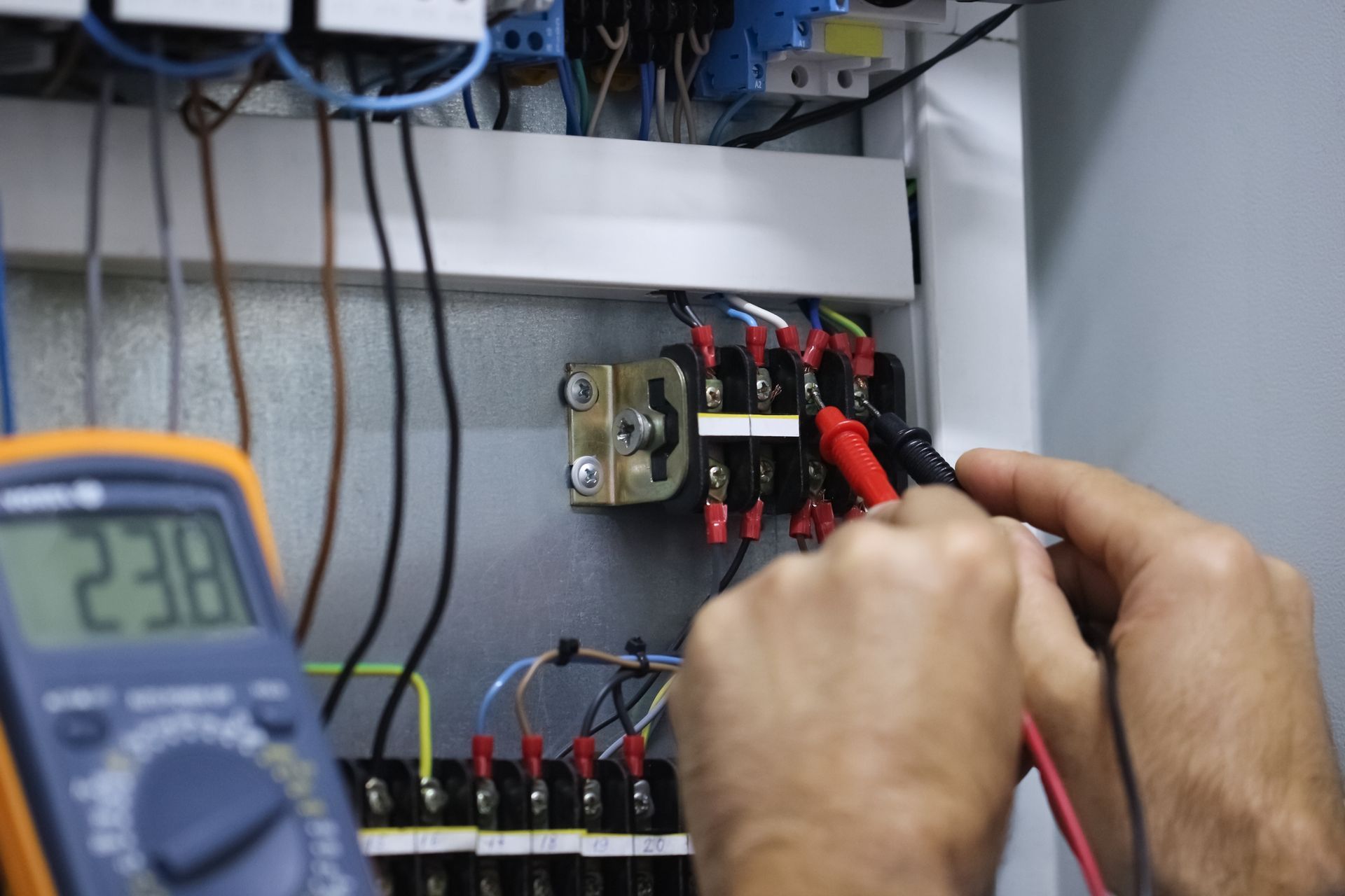 An electrician using a multimeter, working from an open toolbox.