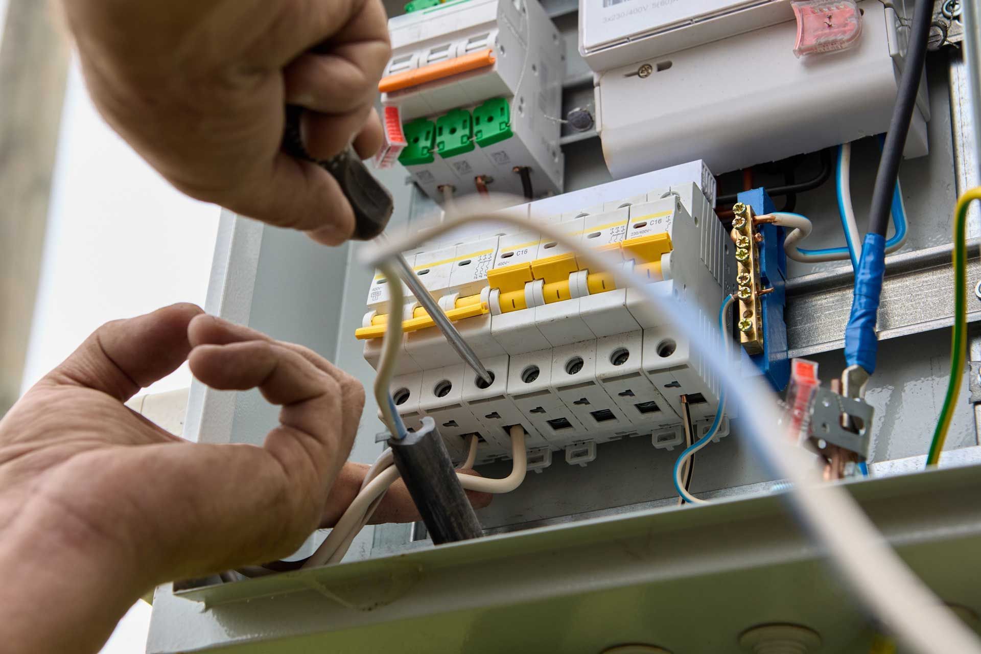 A person is working on an electrical box with a screwdriver.