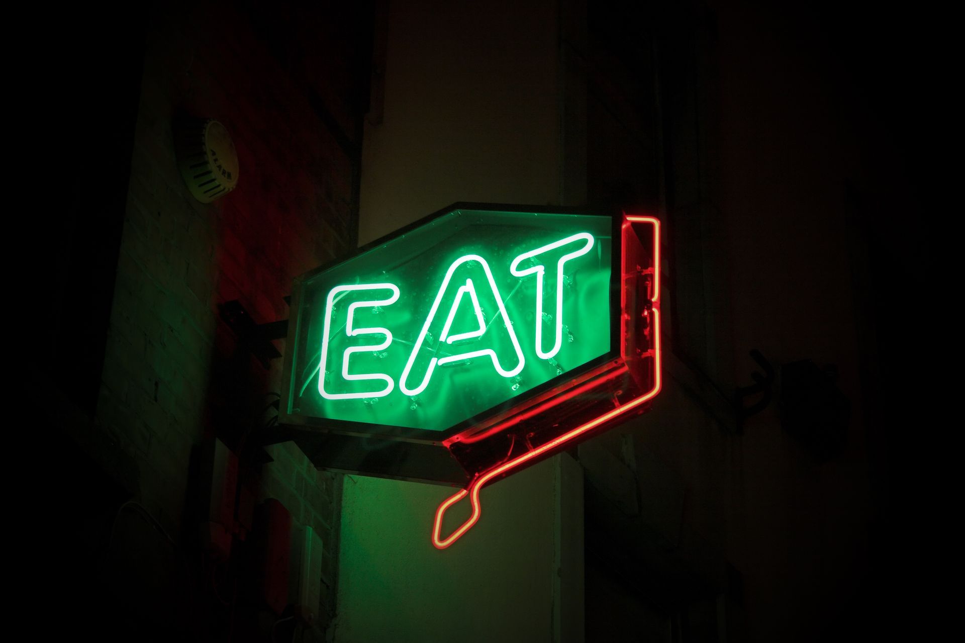A neon sign that says eat is lit up in the dark.