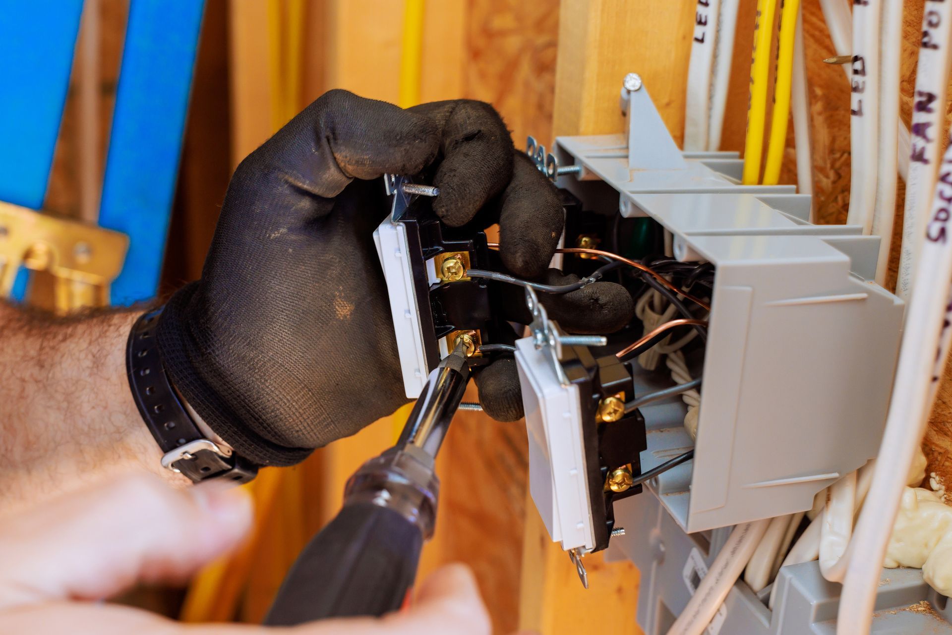 Electrician wearing gloves is connecting electrical switches inside a wall box. Electrician wearing gloves is connecting electrical switches inside a wall box.