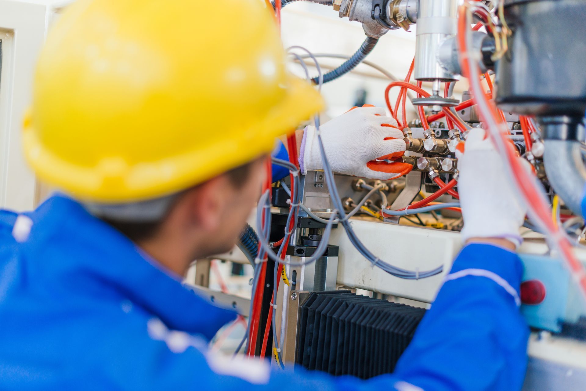 A man wearing an orange hard hat and a yellow vest is working on a machine.