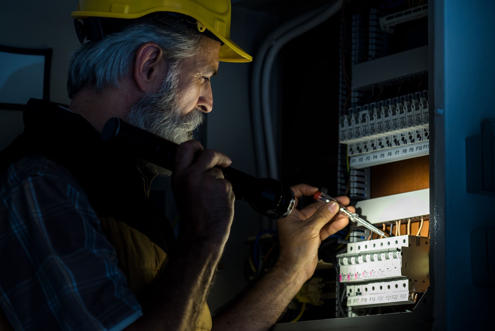 A male emergency electrician checking faulty panel in the dark.