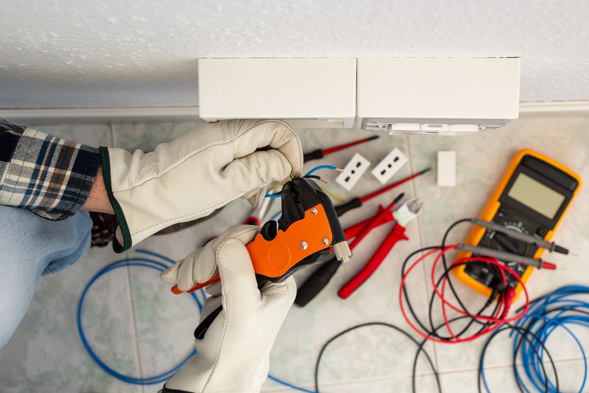 An electrician, in protective gloves, is working with wire stripper pliers on an electrical system.