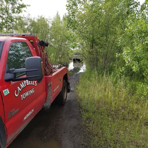 A red tow truck is parked on the side of a dirt road.