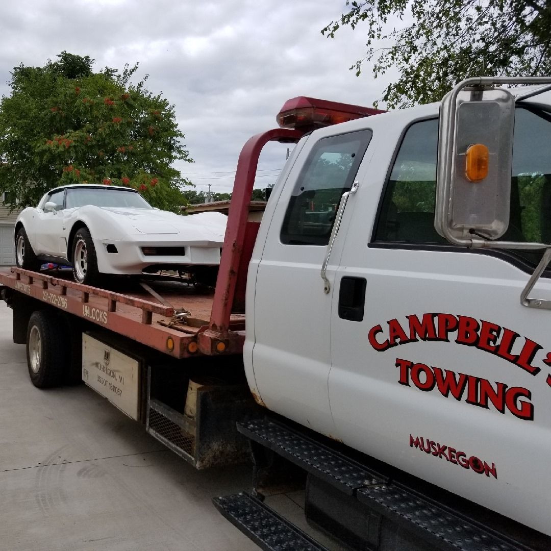 A white car is being towed by a campbell 's towing truck