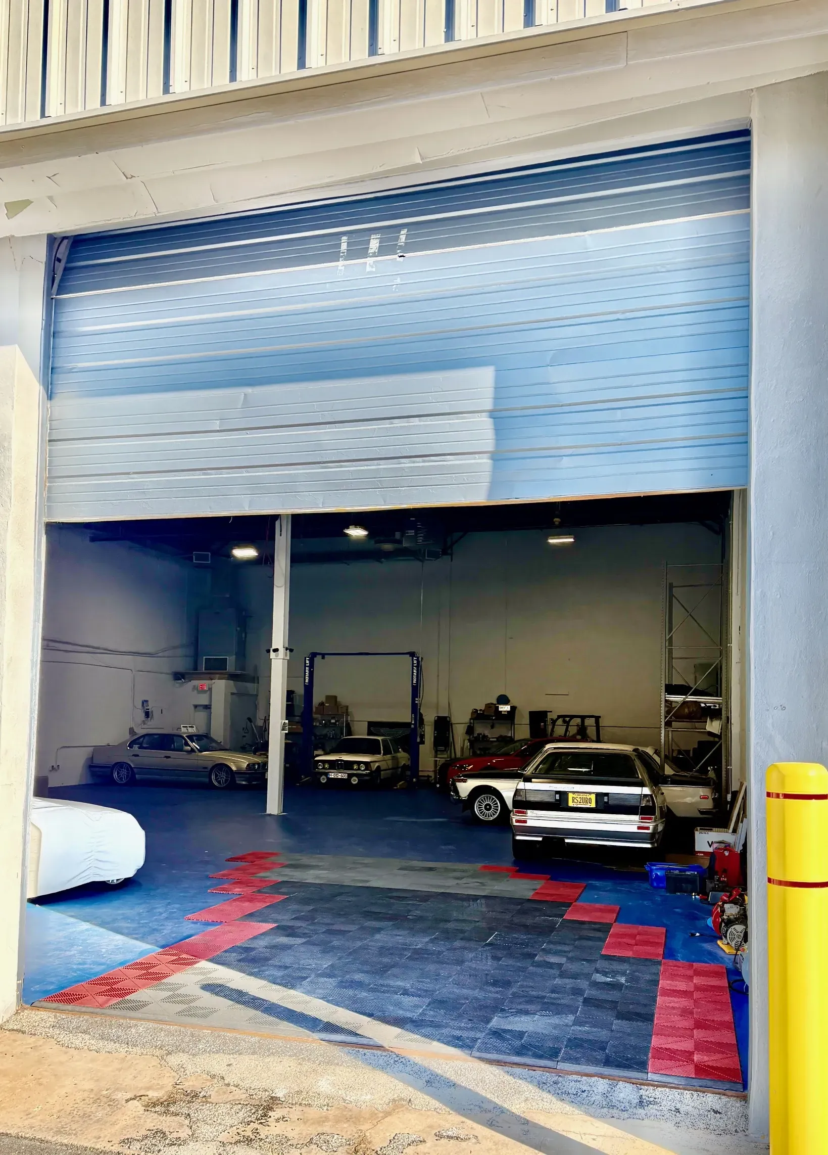 Garage with partially open blue door. Cars and equipment inside.