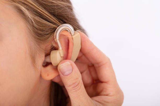 A woman is putting a hearing aid in her ear.
