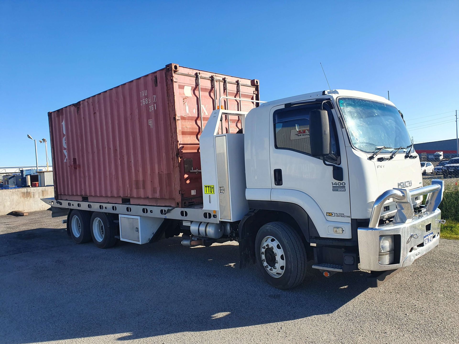 A white truck with a red shipping container on the back is parked in a gravel lot.