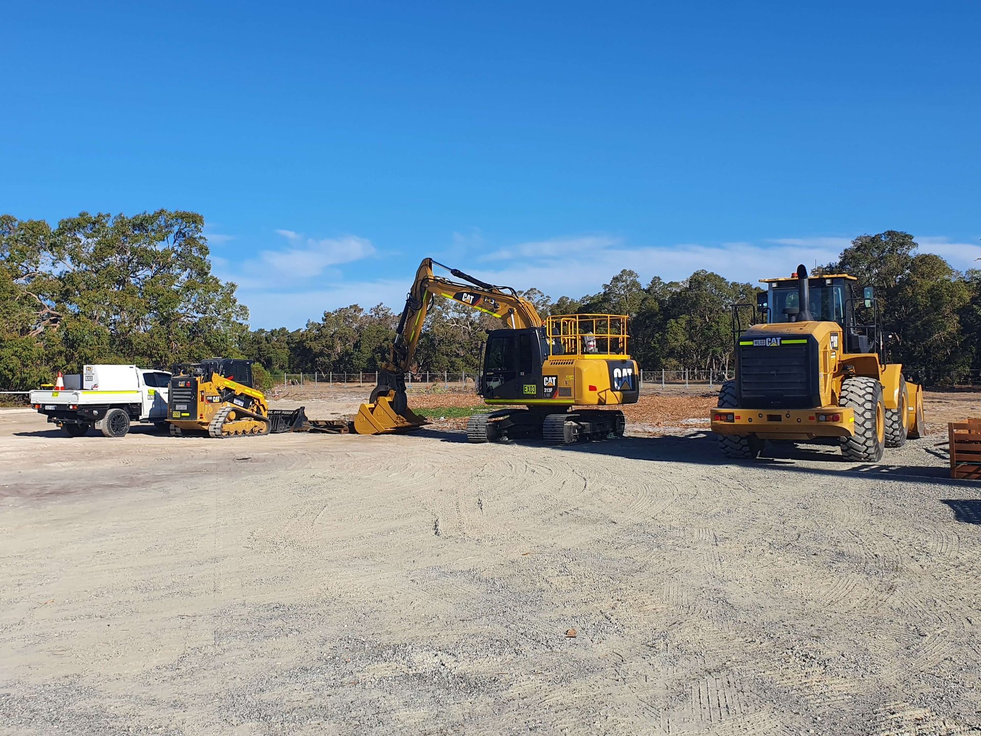 A group of construction vehicles are parked in a gravel lot.