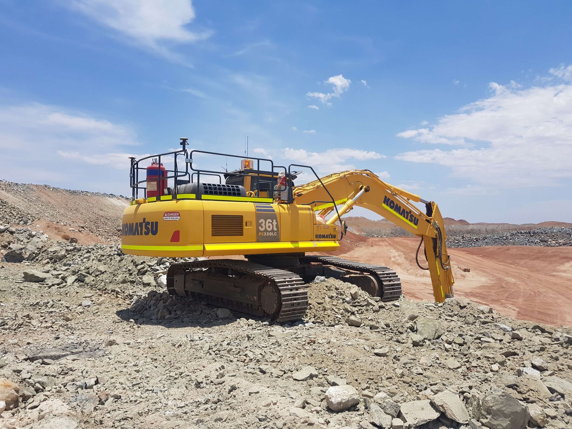 A yellow excavator is sitting on top of a pile of rocks.