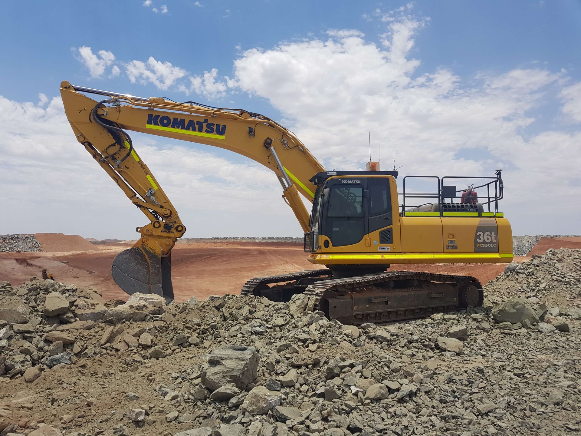 A yellow excavator is sitting on top of a pile of rocks.