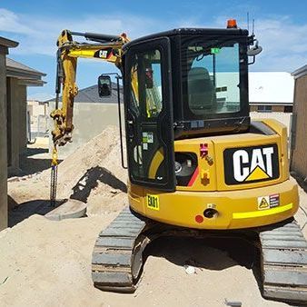 A yellow cat excavator is parked in front of a pile of dirt.