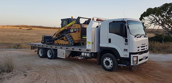 A tow truck is carrying a bulldozer on a dirt road.