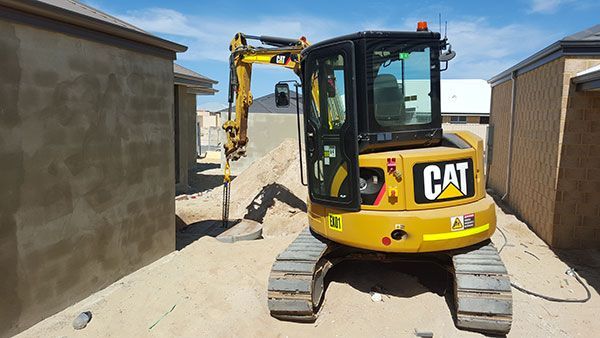 A yellow cat excavator is parked in front of a building.