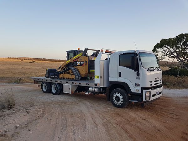 A tow truck with a bulldozer on the back is parked on a dirt road.