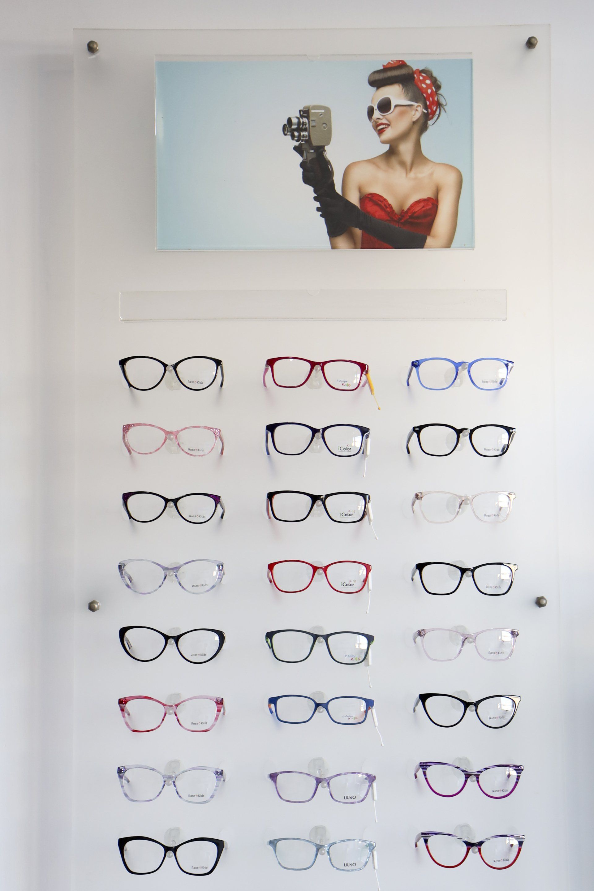 Espositore per occhiali raffigurante una donna retrò con occhiali da sole, appoggiato su una parete bianca.