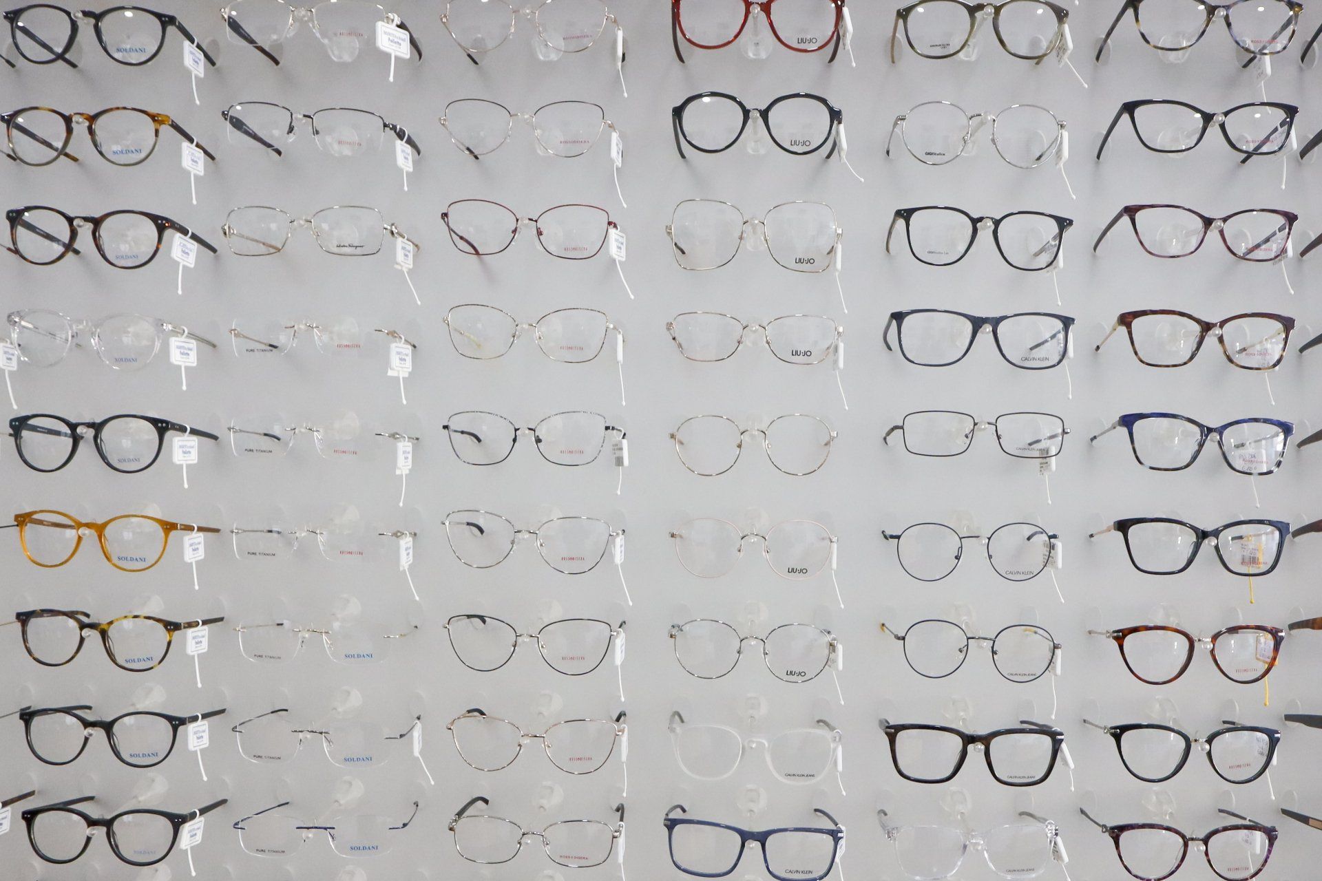 Montature per occhiali disposte su una parete espositiva, che mostrano varie forme e stili, illuminate in un negozio.