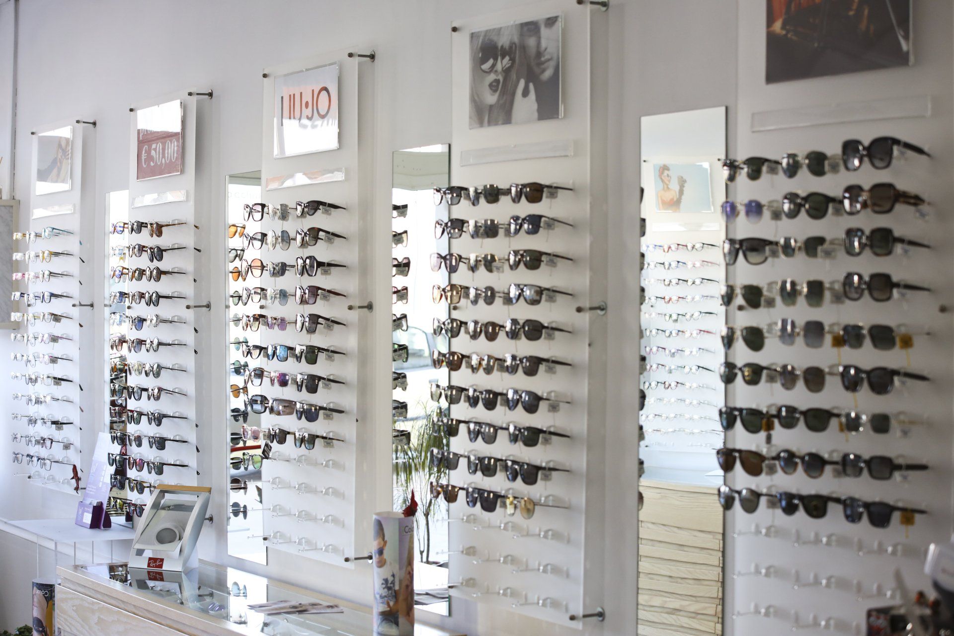 Occhiali da sole esposti su espositori bianchi a parete in un negozio di ottica.