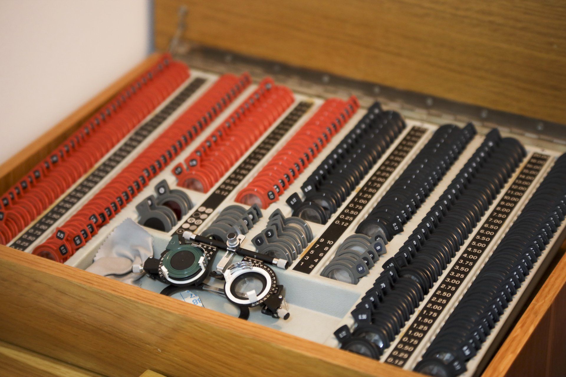 Valigetta in legno contenente lenti rosse e nere per un esame della vista, insieme a una montatura di prova.