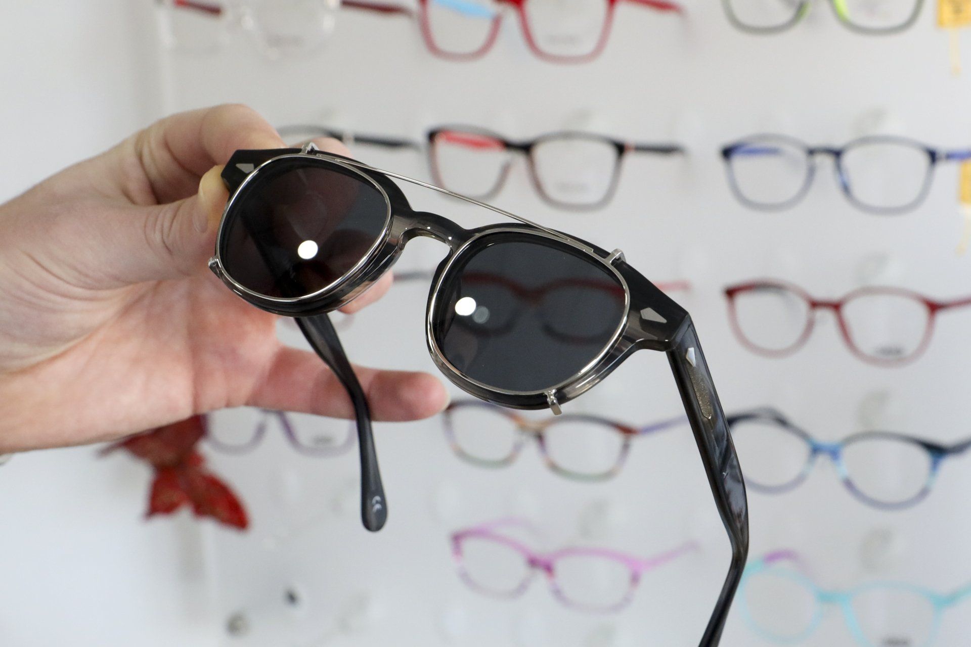 Persona con occhiali da sole neri con lenti circolari, occhiali sullo sfondo.