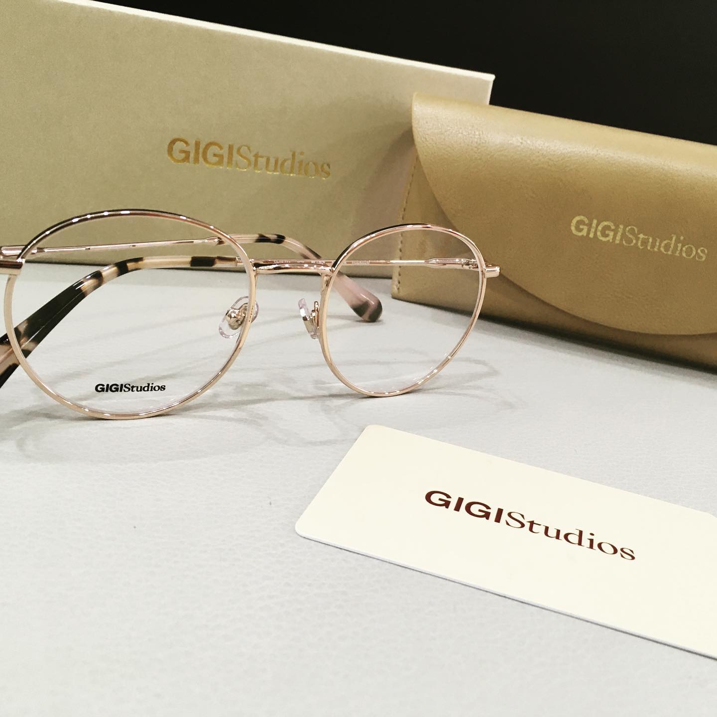 Occhiali da vista, custodia e scatola color oro rosa di GIGIStudios su una superficie bianca.