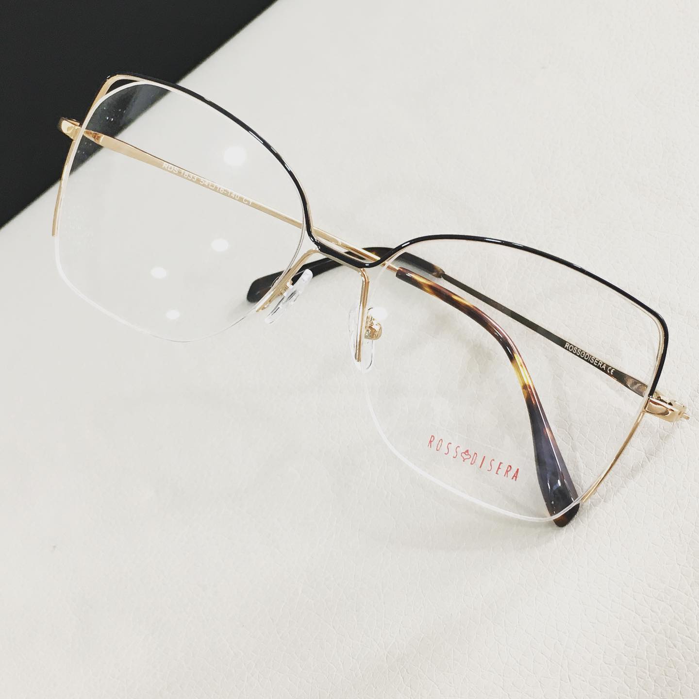 Occhiali con montatura dorata e lenti trasparenti, appoggiati su una superficie bianca.