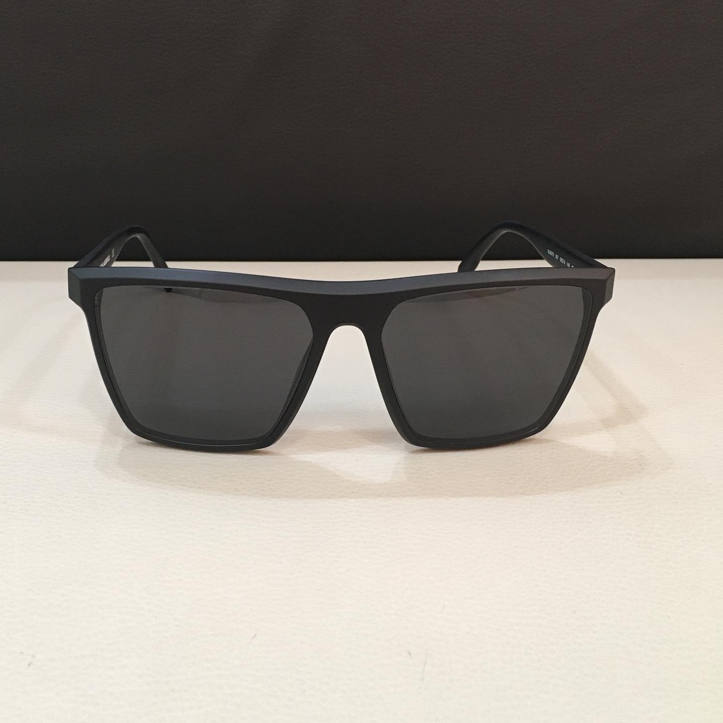 Occhiali da sole neri su una superficie bianca contro uno sfondo scuro.
