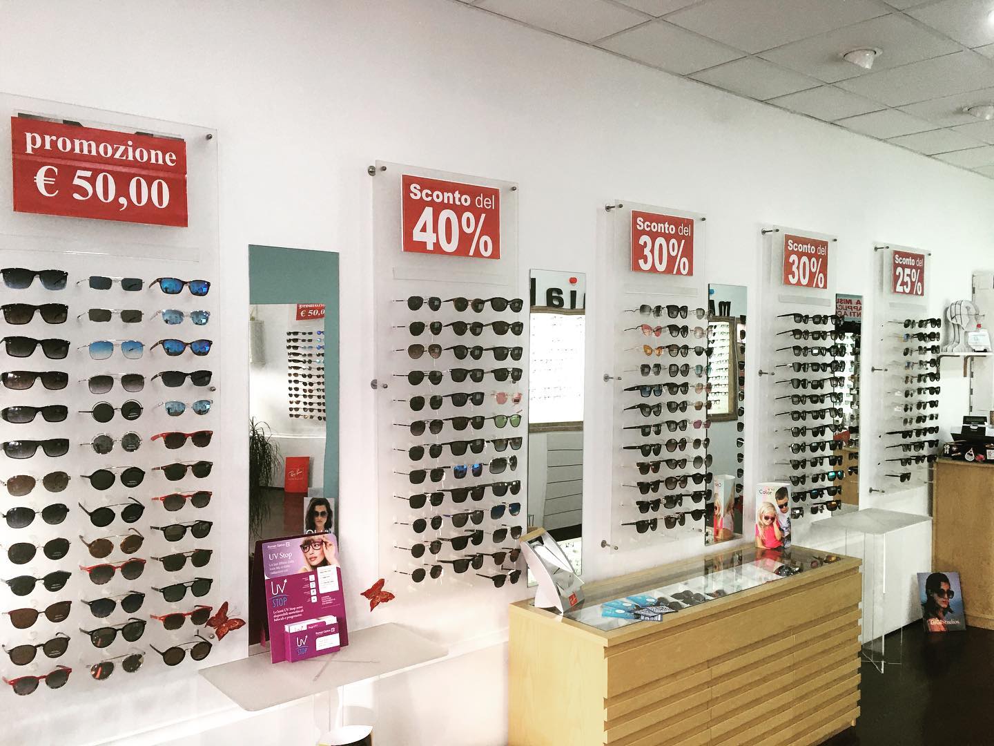 Occhiali da sole esposti in un negozio con cartelli di sconto: 50, 40 e 30 percento di sconto.
