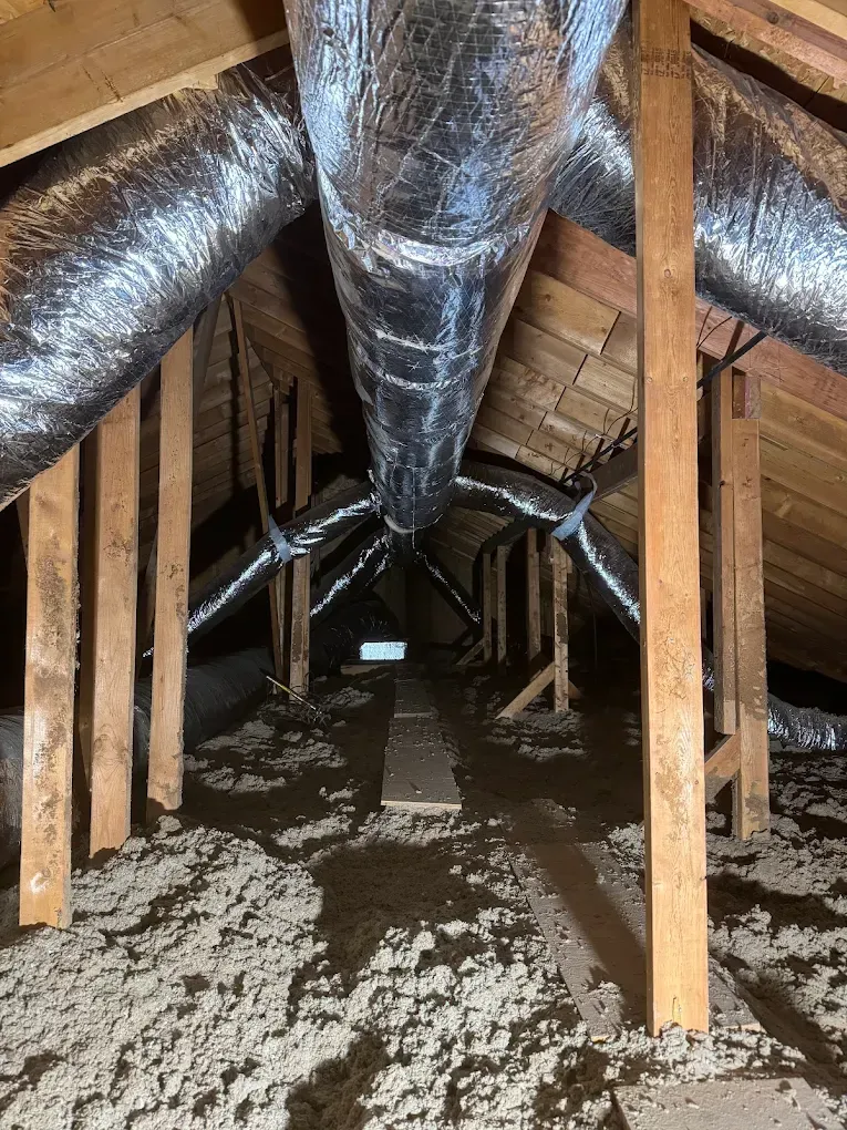 Attic interior with wooden beams, insulated flooring, and flexible HVAC ductwork.