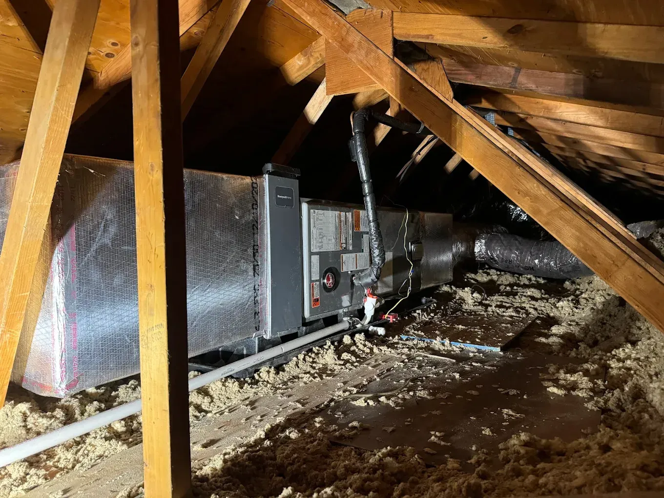 HVAC unit in an attic with wooden beams, insulated ductwork, and insulation on the floor.