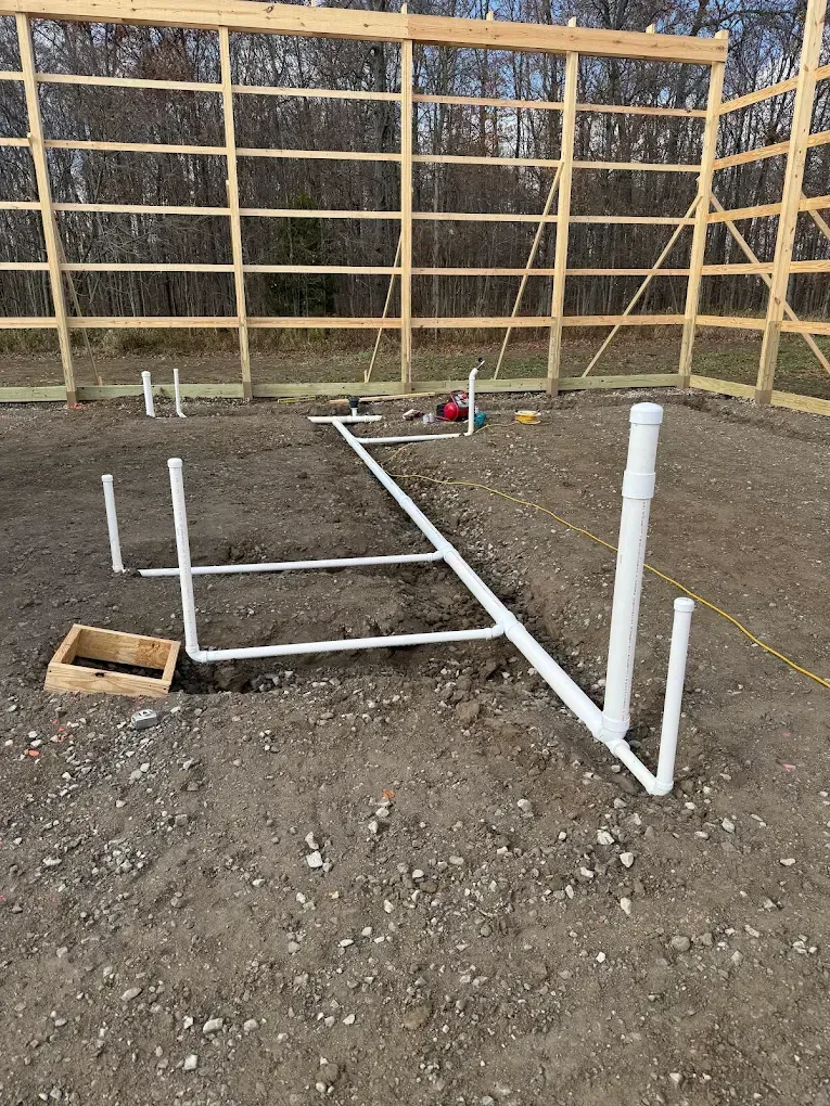 PVC plumbing pipes installed on dirt ground at a construction site, with wooden framing visible in the background.