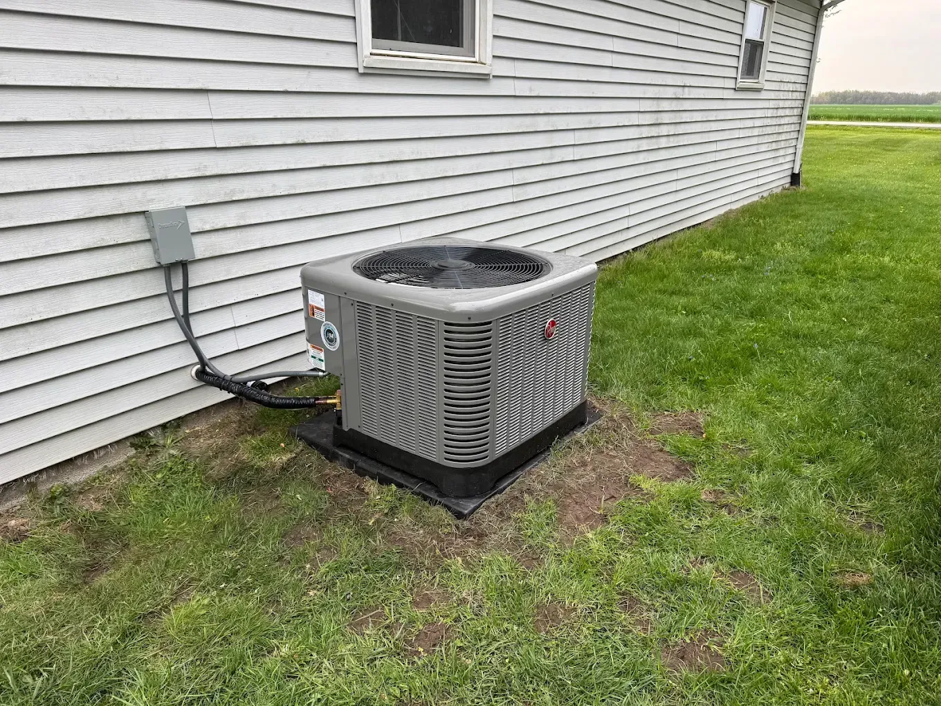 Outdoor air conditioning unit beside a white house, on a grassy lawn.
