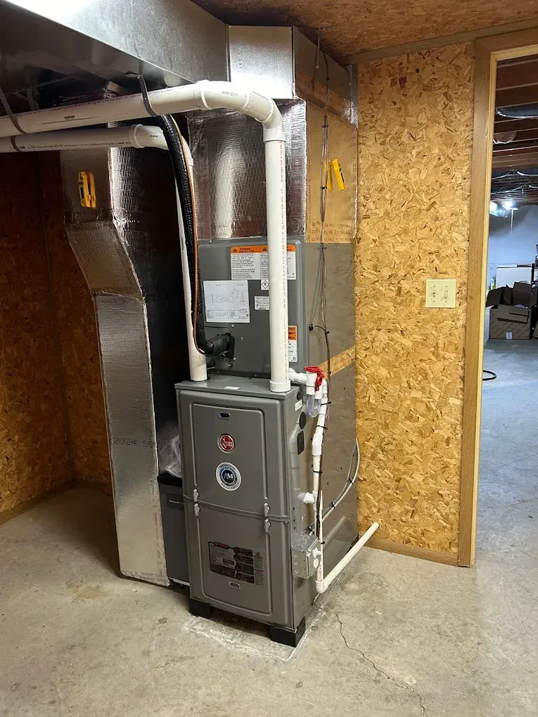 Furnace unit with ductwork installed against a wood-paneled wall in a basement setting.