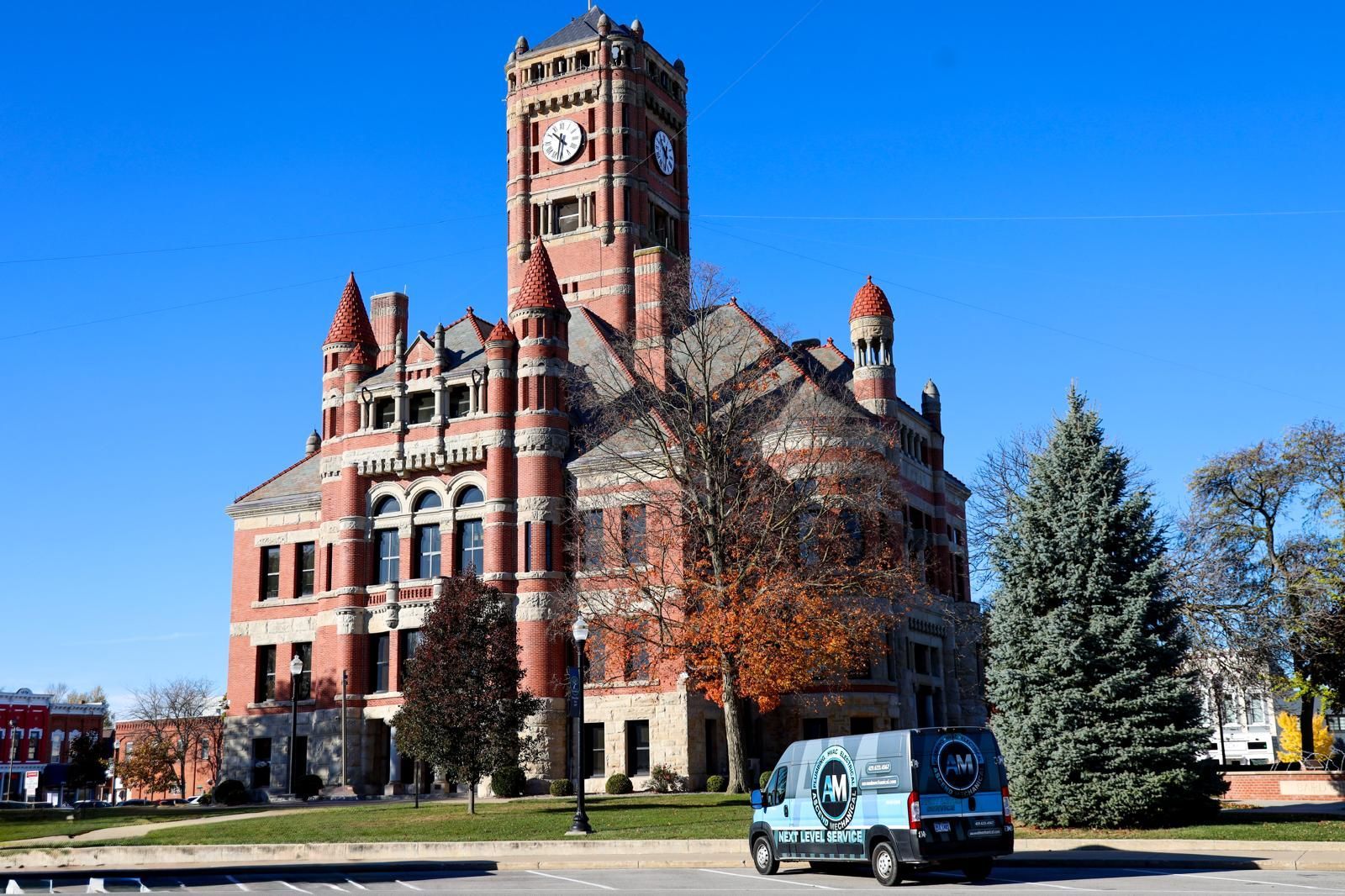 Red brick courthouse with clock tower; a van parked in front on a sunny day.