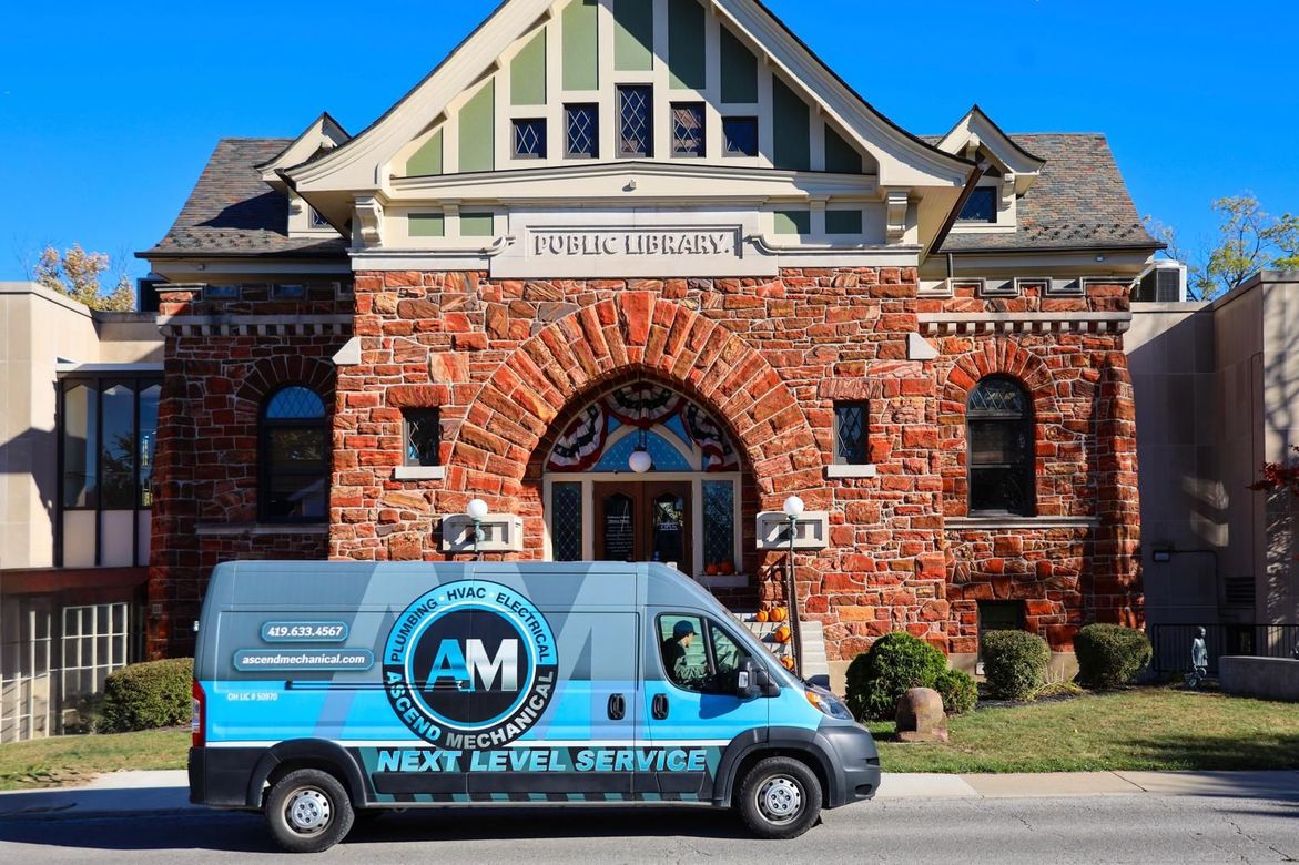 Blue and gray service van parked in front of a brick library. The van has the company logo