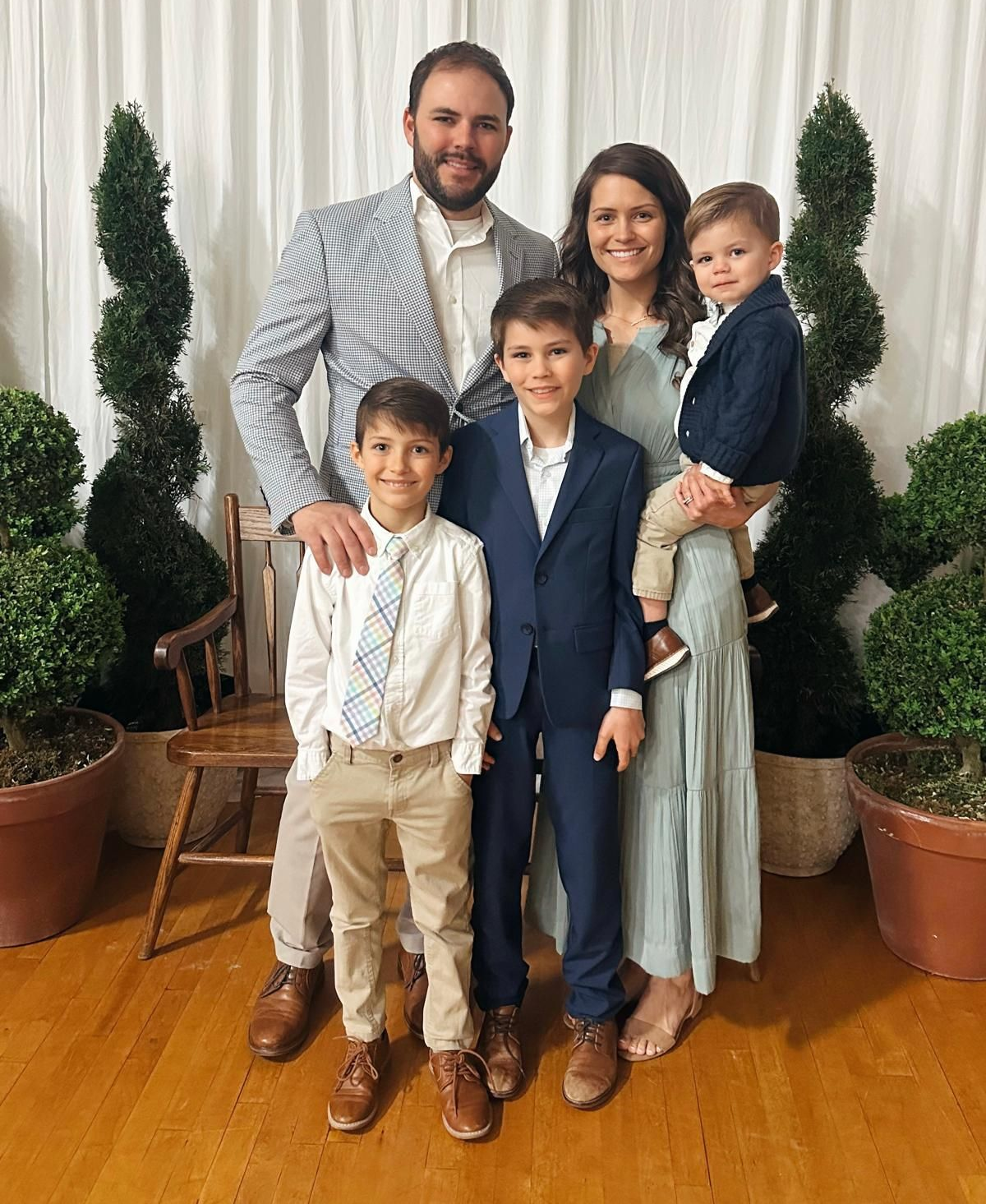 Family of five smiling, posing indoors. Father in seersucker jacket, mother in dress, three boys in suits.