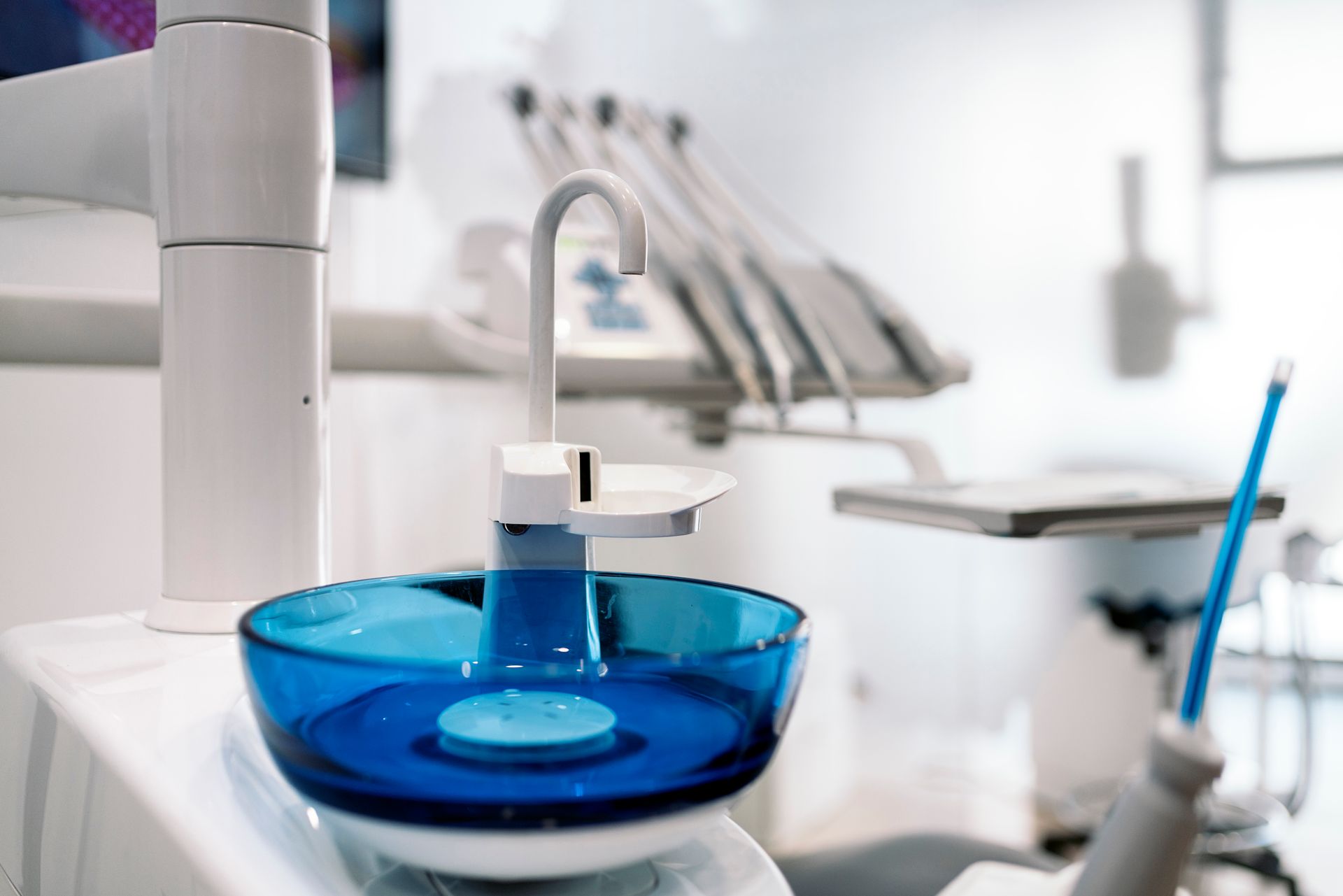 Dental chair with equipment, including a blue bowl and water spout, in a bright dental office.