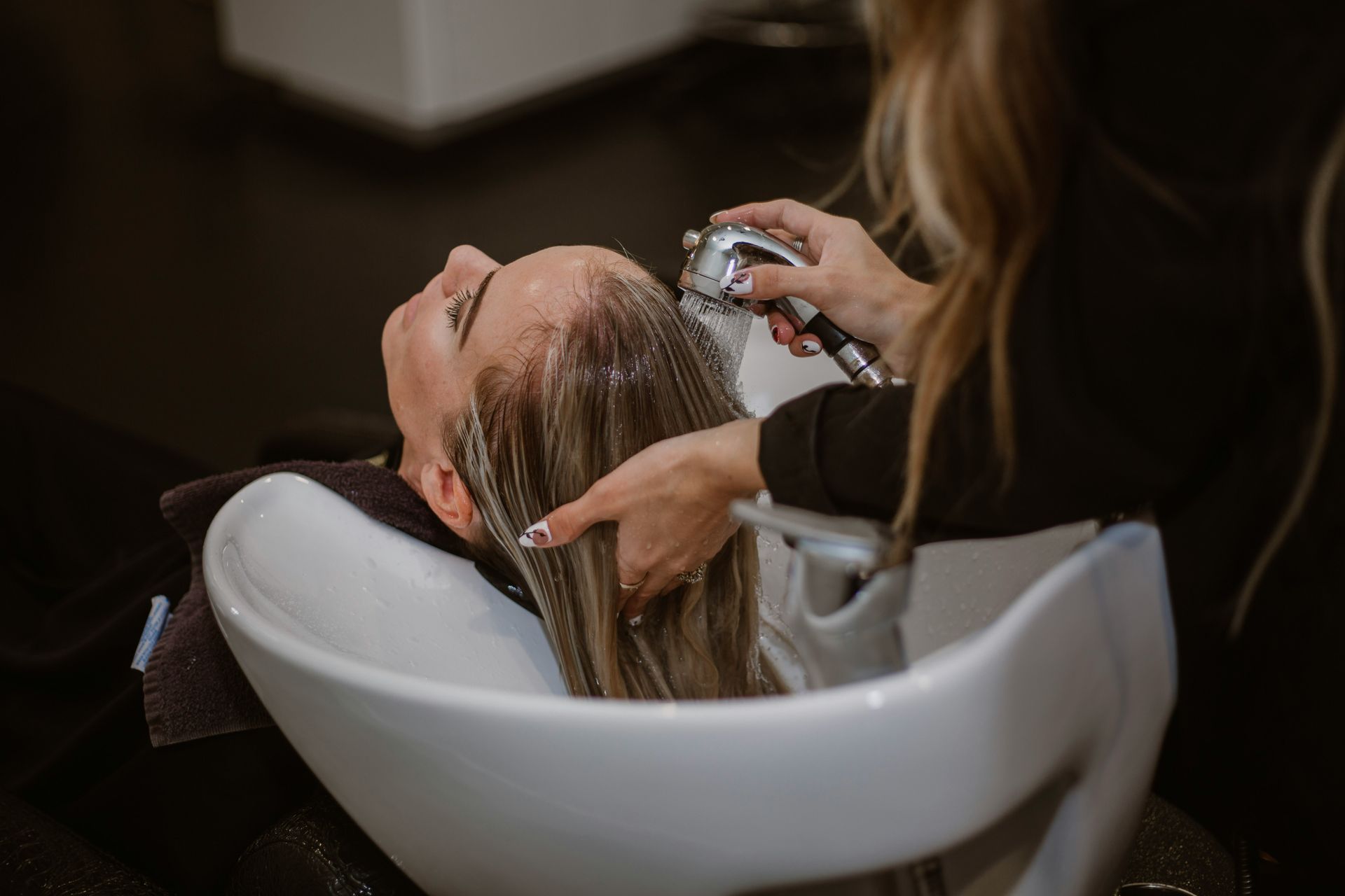 Person having hair washed at a salon, head in white basin.