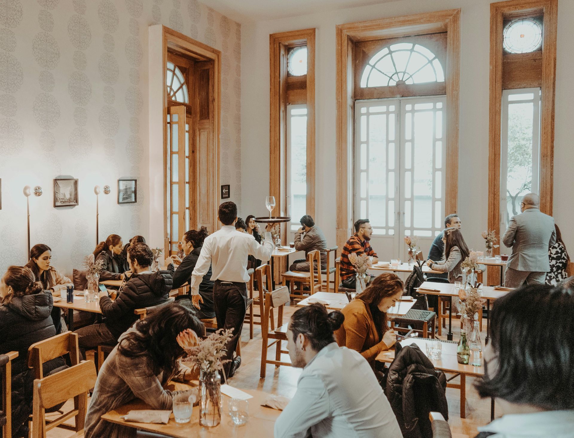 People in a bright room with wooden tables and chairs, attending a meeting or event.