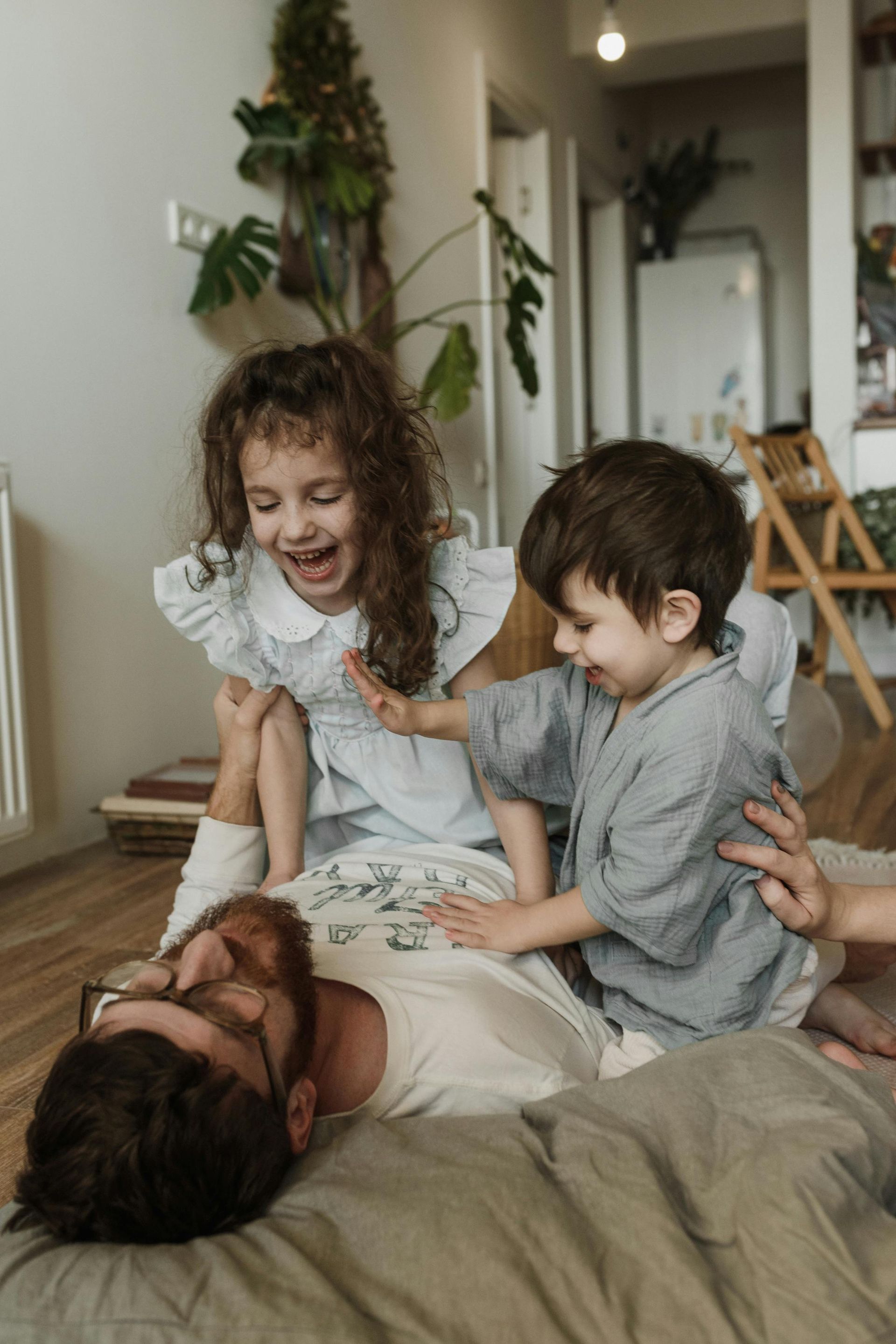 Man lying on a bed with two children playing and laughing on top of him.