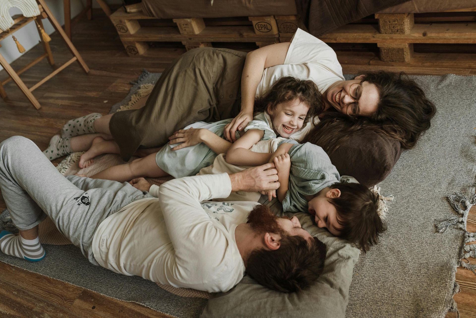 Family of four, smiling and laughing, lying together on a rug in a room.
