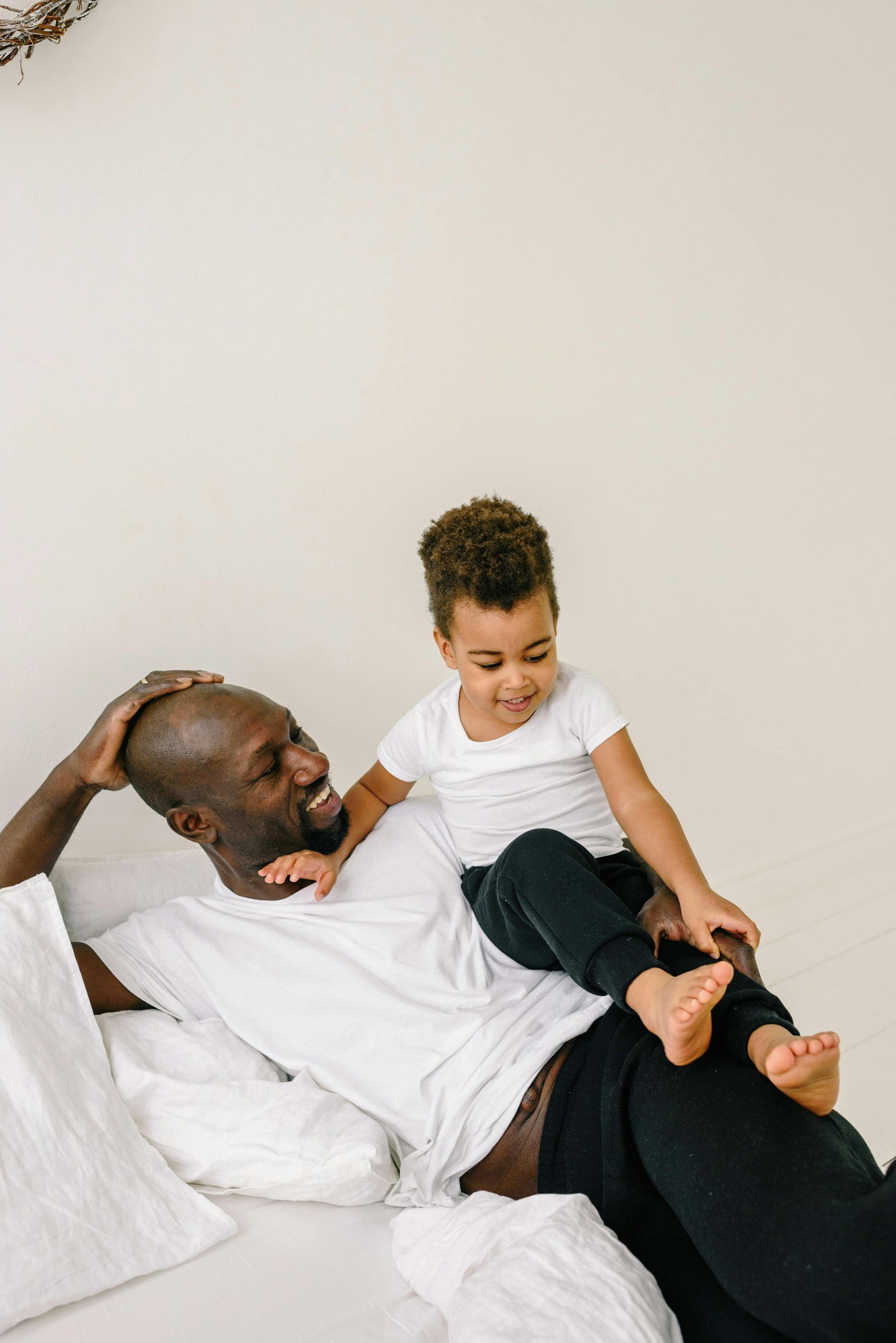 Man lying down with child on top; both are smiling in a white room.