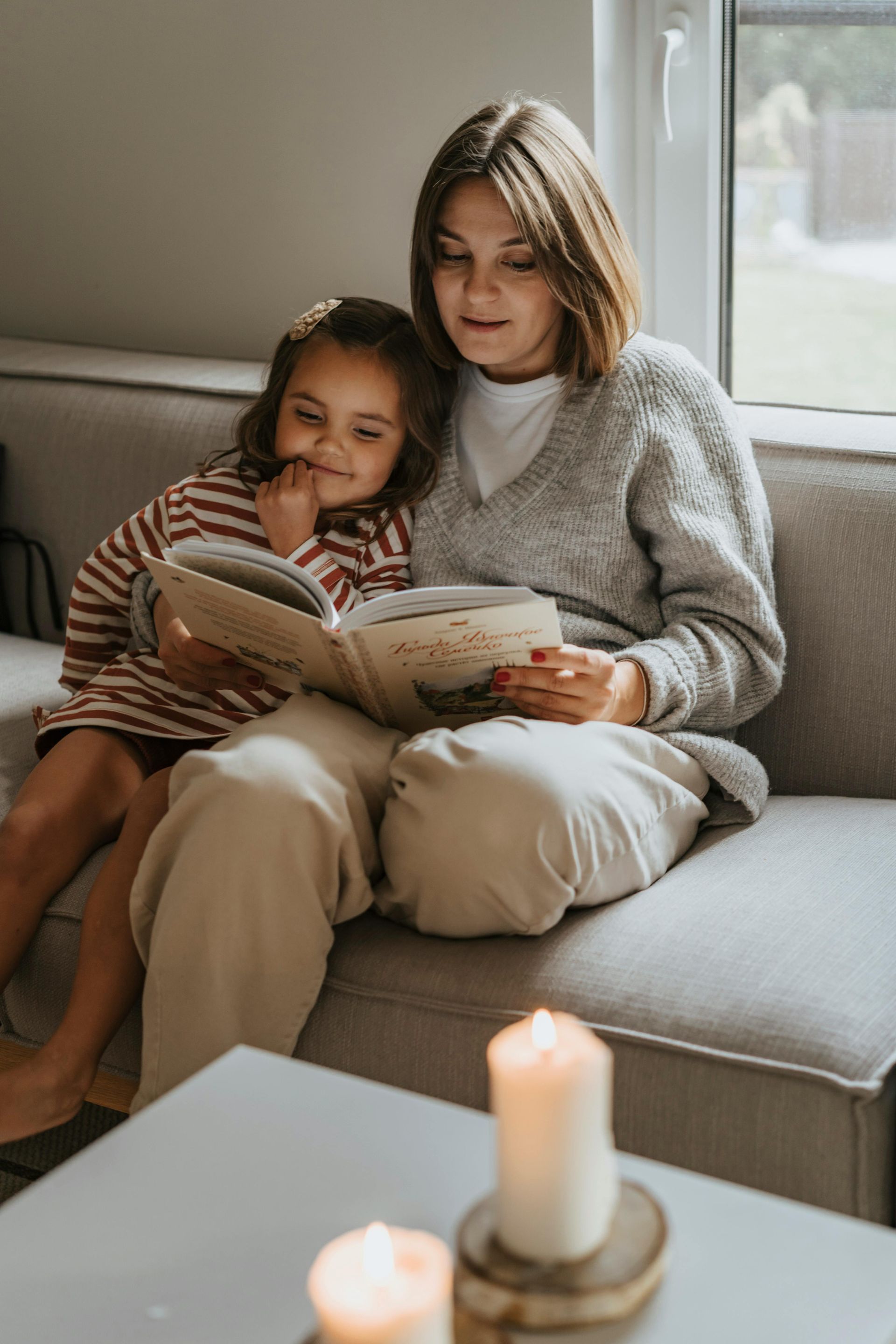 Woman and child reading a book on a couch, with candles nearby.