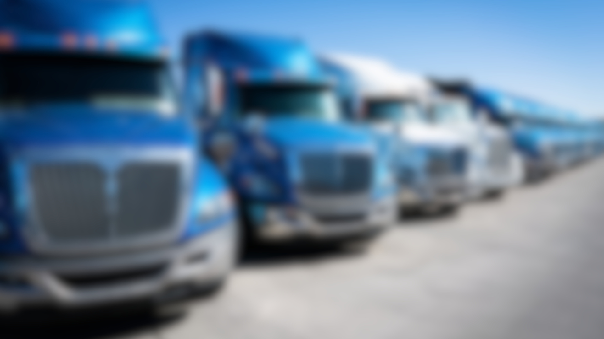 A row of blue semi trucks are parked in a parking lot.